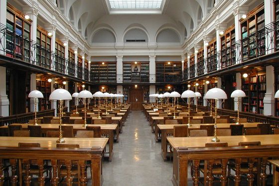University library reading room with wooden desks, white reading lamps and two floors of bookshelves