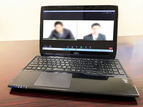 Laptop on a desk showing a video conference with two pixelated participants