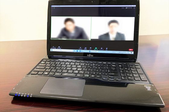 Laptop on a desk showing a video conference with two pixelated participants