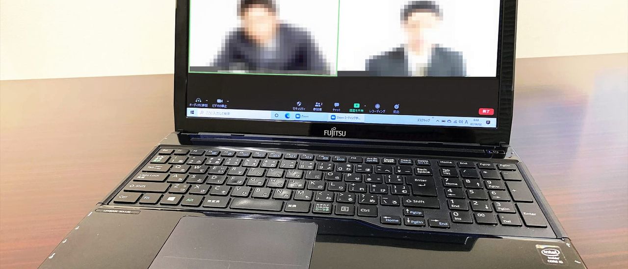 Laptop on a desk showing a video conference with two pixelated participants