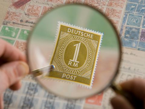 Hand holding a magnifying glass over an old German postage stamp in a collection