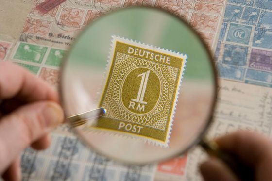 Hand holding a magnifying glass over an old German postage stamp in a collection