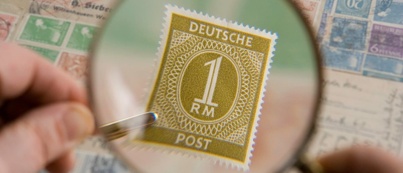 Hand holding a magnifying glass over an old German postage stamp in a collection