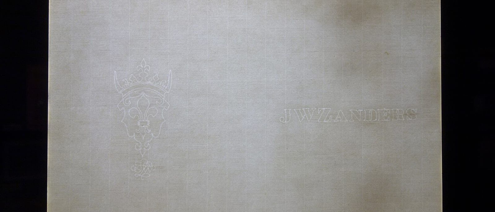 Sheet of laid paper on a light box showing a crowned crest watermark and a maker's name