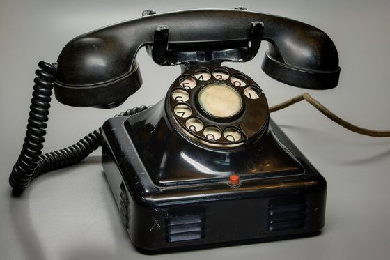 Black Bakelite rotary telephone with coiled cord on a grey background