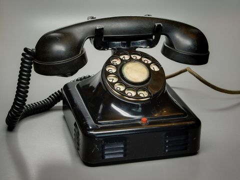 Black Bakelite rotary telephone with coiled cord on a grey background