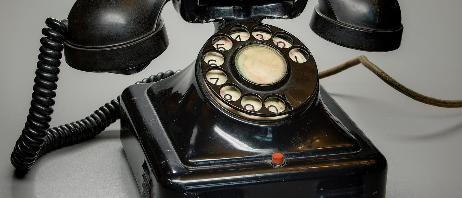 Black Bakelite rotary telephone with coiled cord on a grey background