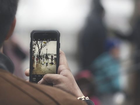 Person photographing a rainy riverside street scene with a smartphone camera