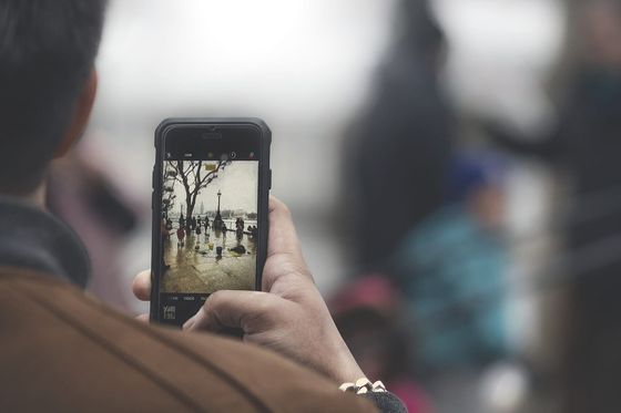Person photographing a rainy riverside street scene with a smartphone camera