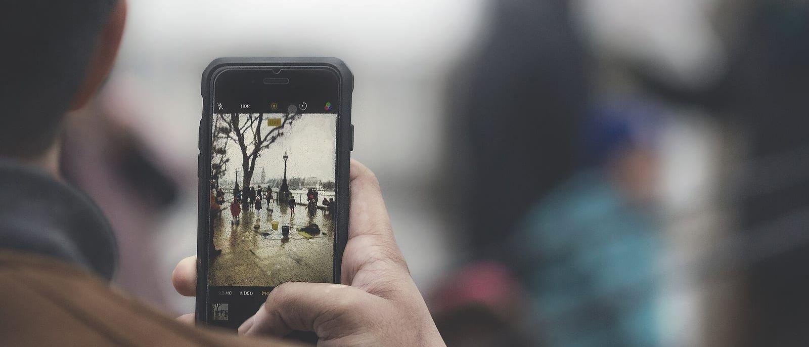 Person photographing a rainy riverside street scene with a smartphone camera