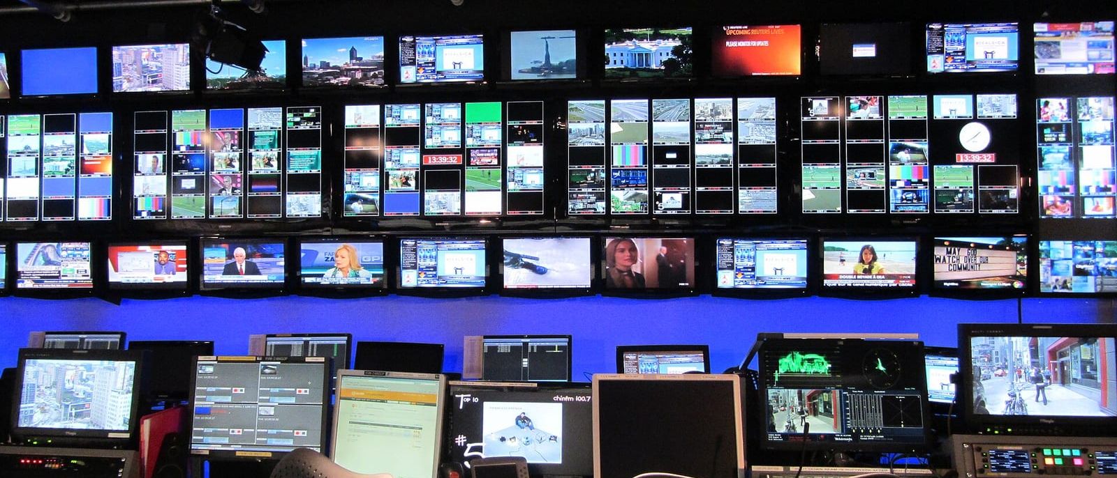 Wall of broadcast monitors and control desks in a television station control room